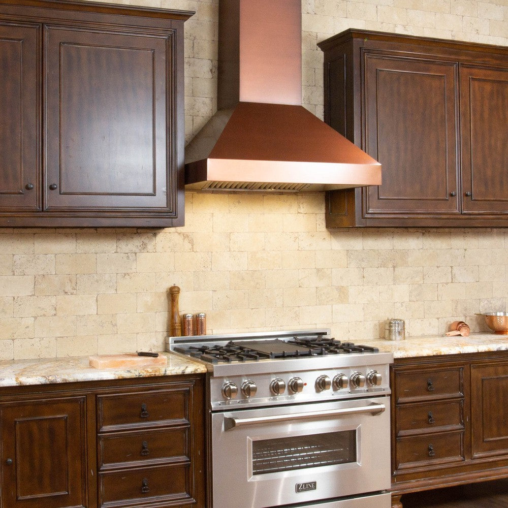 ZLINE Convertible Designer Series Copper Wall Mount Range Hood (8667C) in a rustic-style kitchen with brown cabinets  with cooktop lighting on.