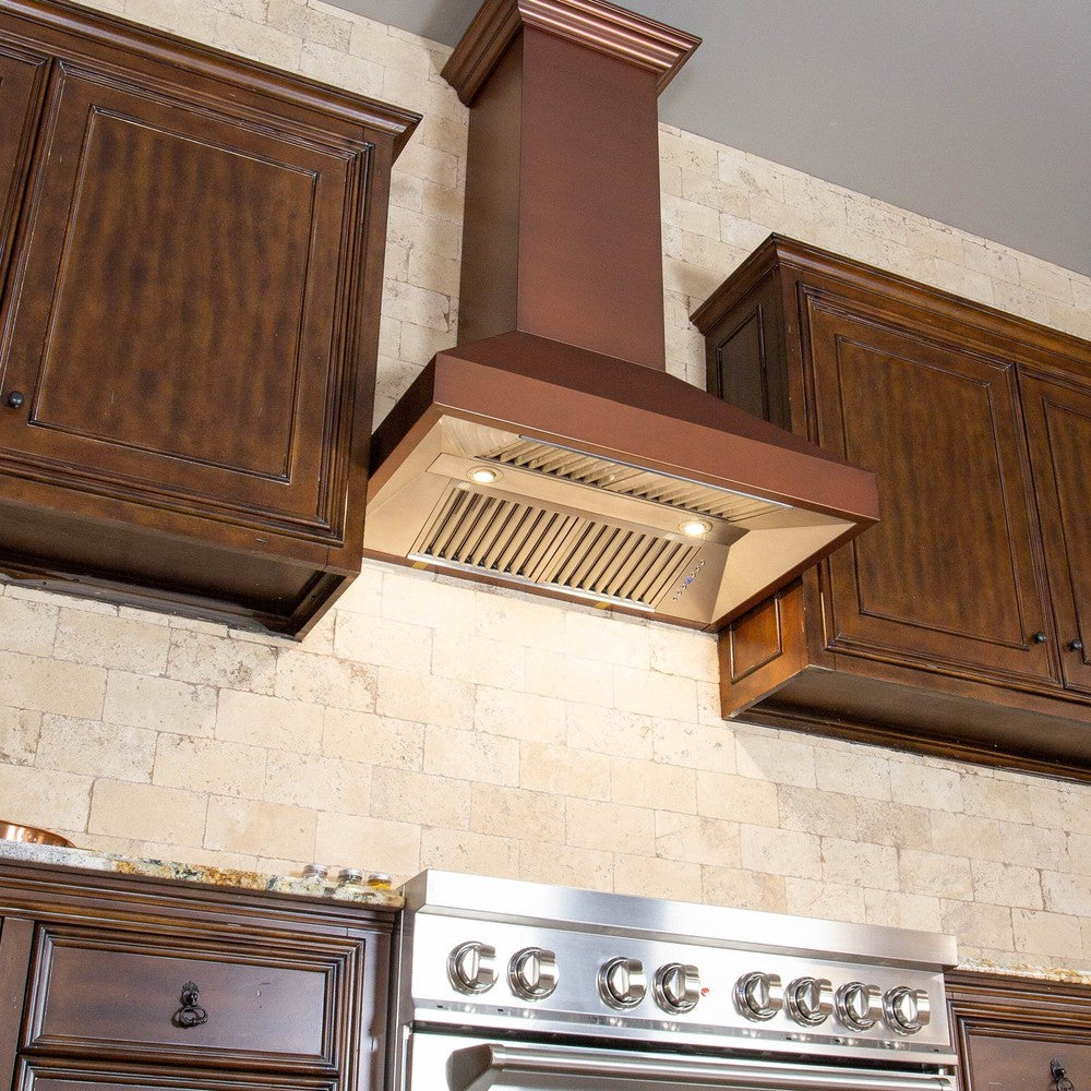 ZLINE Convertible Designer Series Copper Wall Mount Range Hood (8667C) in a rustic-style kitchen with brown cabinets from below with cooktop lighting on.