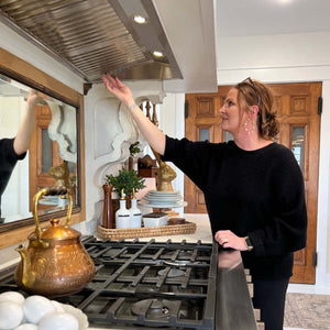 Woman in a kitchen adjusting a ZLINE 40 in. Ducted Wall Mount Range Hood Insert in Outdoor Approved Stainless Steel (698-304-40) in a custom range hood above a cooktop.