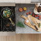 Stovetop with pan of food and kitchen counter with cutting board, knife, and vegetables.