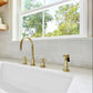 Kingston Brass Concord 8 in. Widespread Kitchen Faucet with Brass Sprayer (KS8726DXBS) in Brushed Brass on a kitchen sink with a window in the background