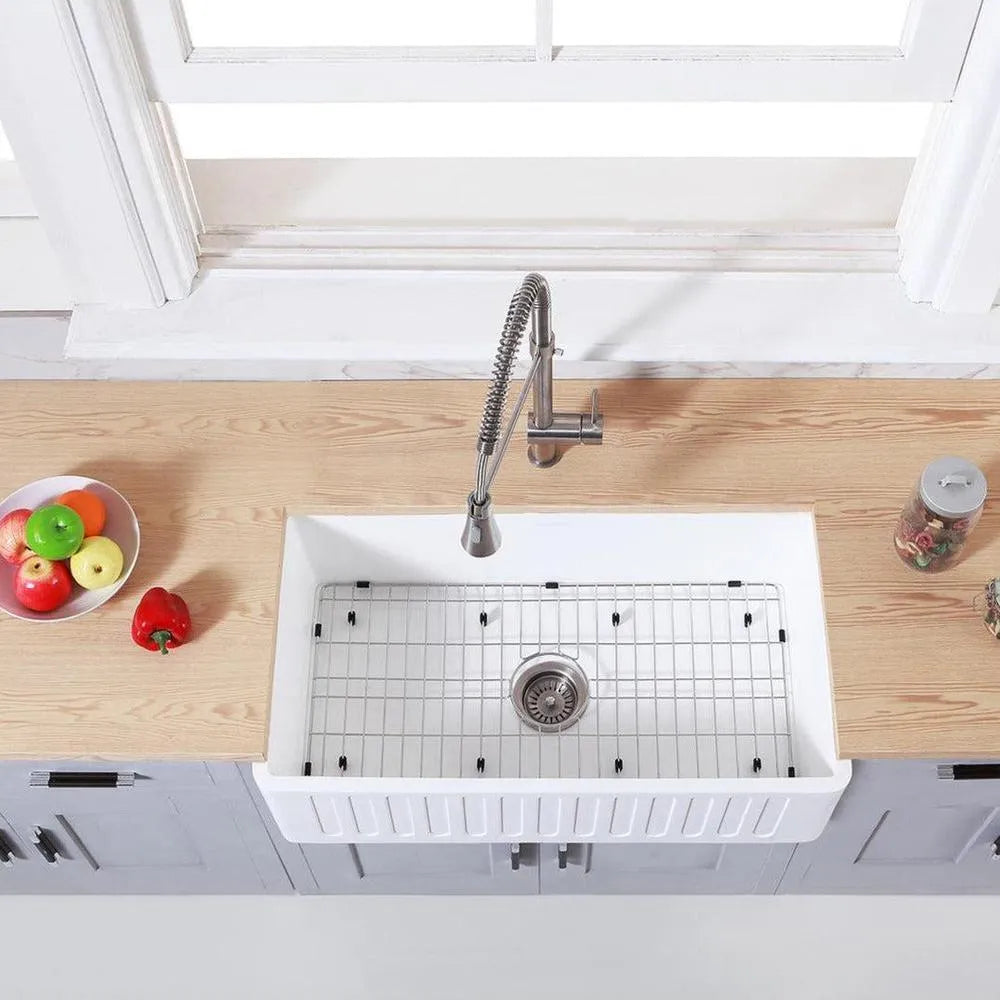 Kingston Brass 33 in. Solid Surface White Stone Apron-Front Single Bowl Farmhouse Kitchen Sink with Strainer and Grid in Matte White (KGKFA331810RM) on a wooden countertop