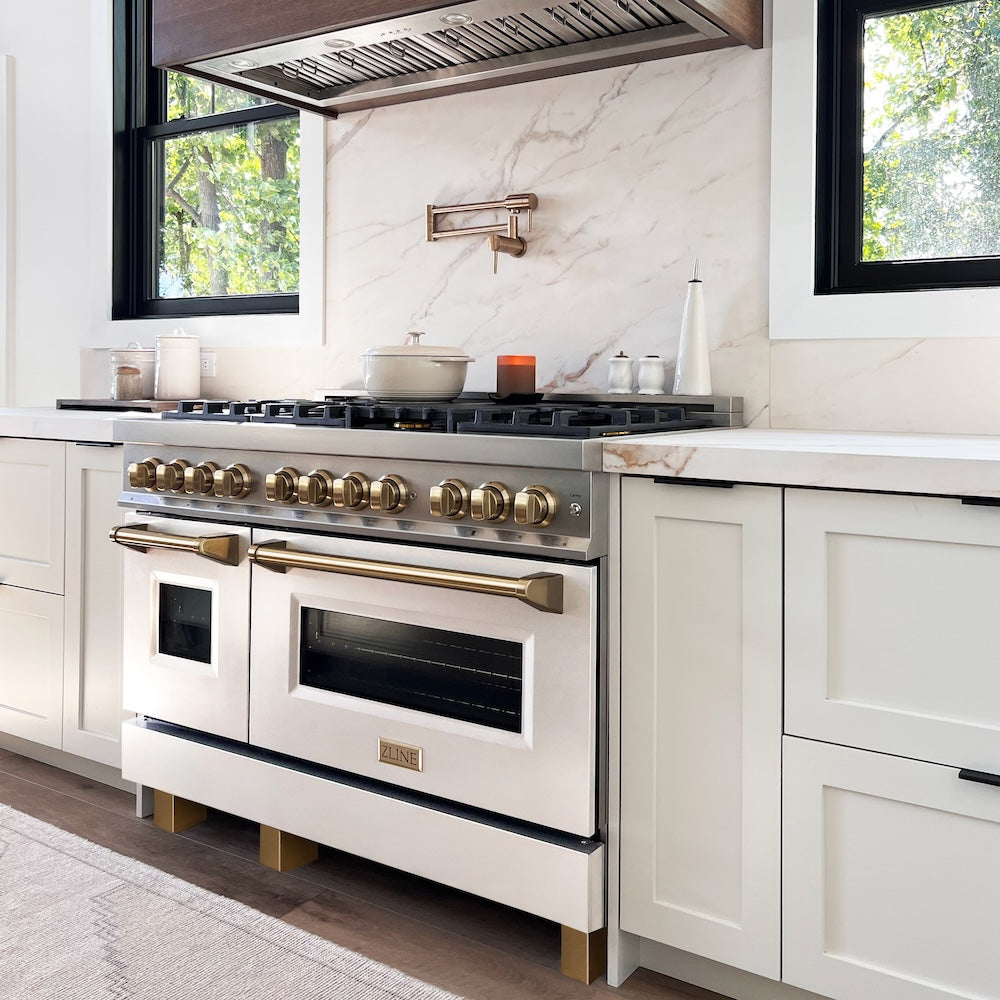 Farmhouse kitchen with a ZLINE Autograph Edition 48 in. 6.0 cu. ft. Legacy Dual Fuel Range with 7 Burner Gas Cooktop and 2 Electric Ovens in Stainless Steel with White Matte Doors and Champagne Bronze Accents (RAZ-WM-48-CB) and marble backsplash