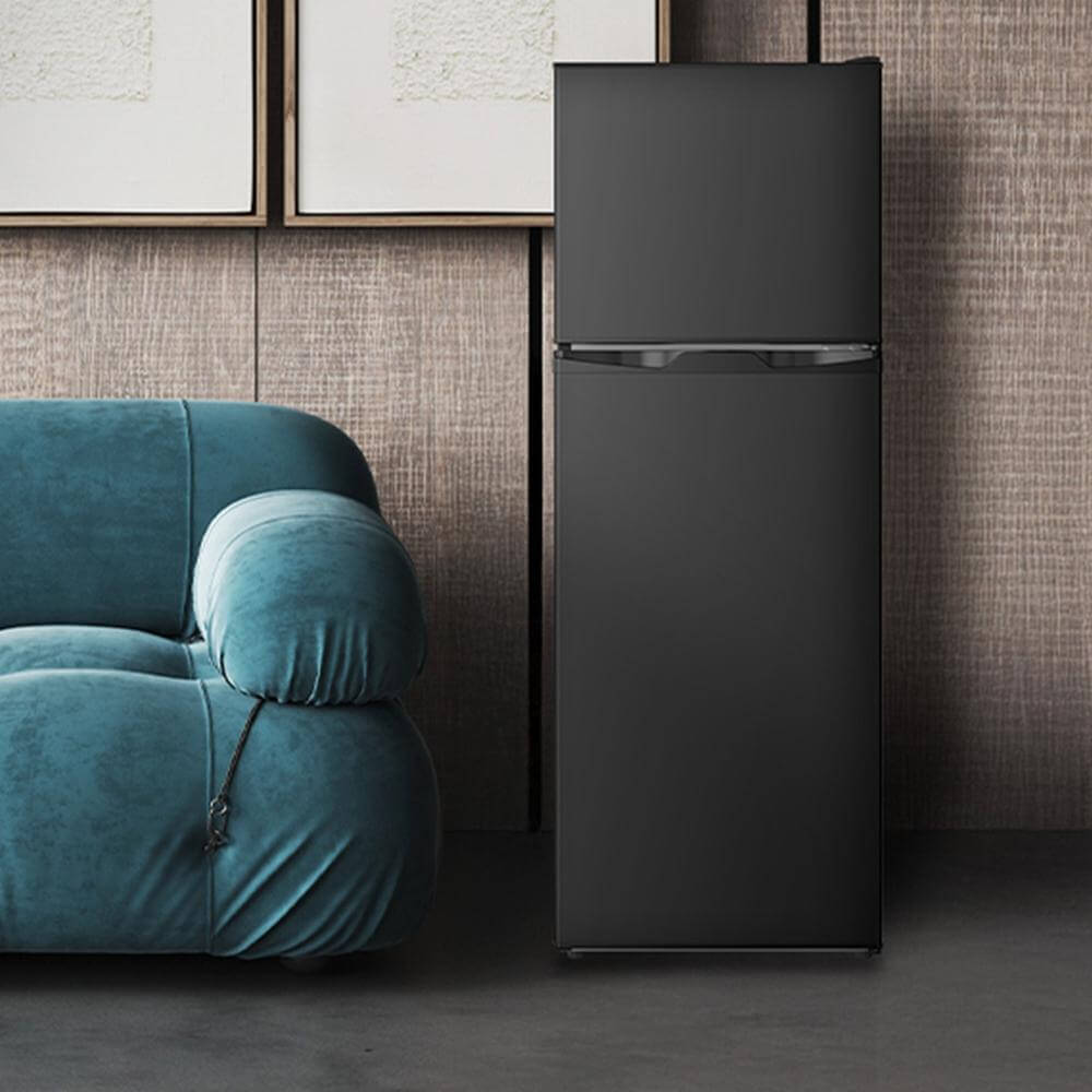 TCL 18 in. 4.7 Cu. Ft. Compact Top Freezer Mini Fridge in Black (TRM47D5AB) next to a blue armchair against a textured wall.