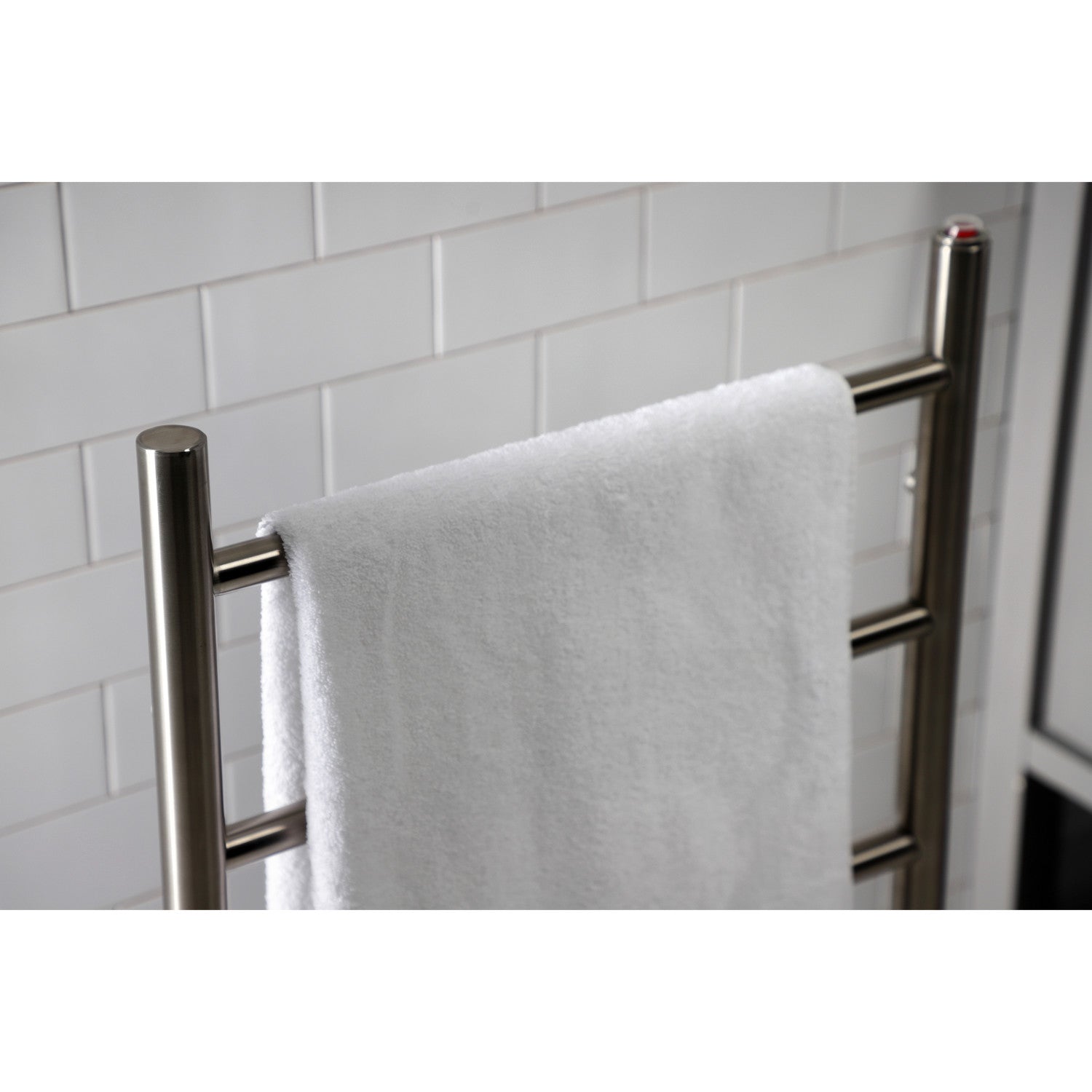 White towel hanging on Kingston Brass Templeton Freestanding/Wall Mount Hardwired or Plug-In Towel Warmer Brushed Nickel against a white tiled wall.