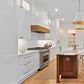 A bright, modern kitchen and dining area with white cabinetry, light wood flooring, a central wooden island, and a small dining table with dark green chairs near a large window.