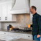 A man standing in a bright kitchen with a white curved range hood.