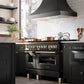 Modern kitchen with ZLINE Autograph Edition 48 in. 6.0 cu. ft. Legacy Dual Fuel Range with 7 Burner Gas Cooktop and 2 Electric Ovens in Black Stainless Steel and Polished Gold Accents (RABZ-48-G) and hood, white tiled walls, and wooden utensils.