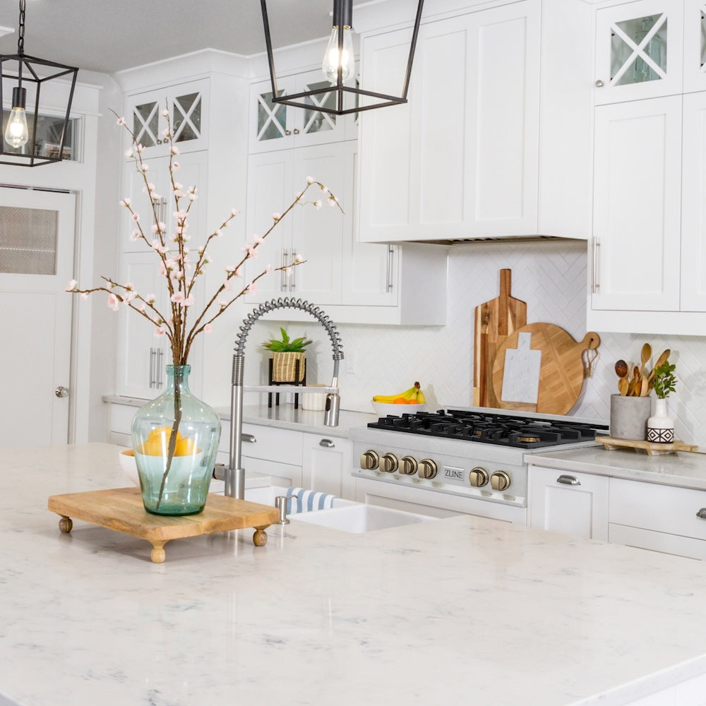 ZLINE Autograph Edition 36 in. Legacy Gas Rangetop with 6 Burners and Porcelain Cooktop in Satin Stainless Steel with Champagne Bronze Accents (RTSZ-36-CB) in a kitchen with white cabinets, marble countertop, and decorative elements.