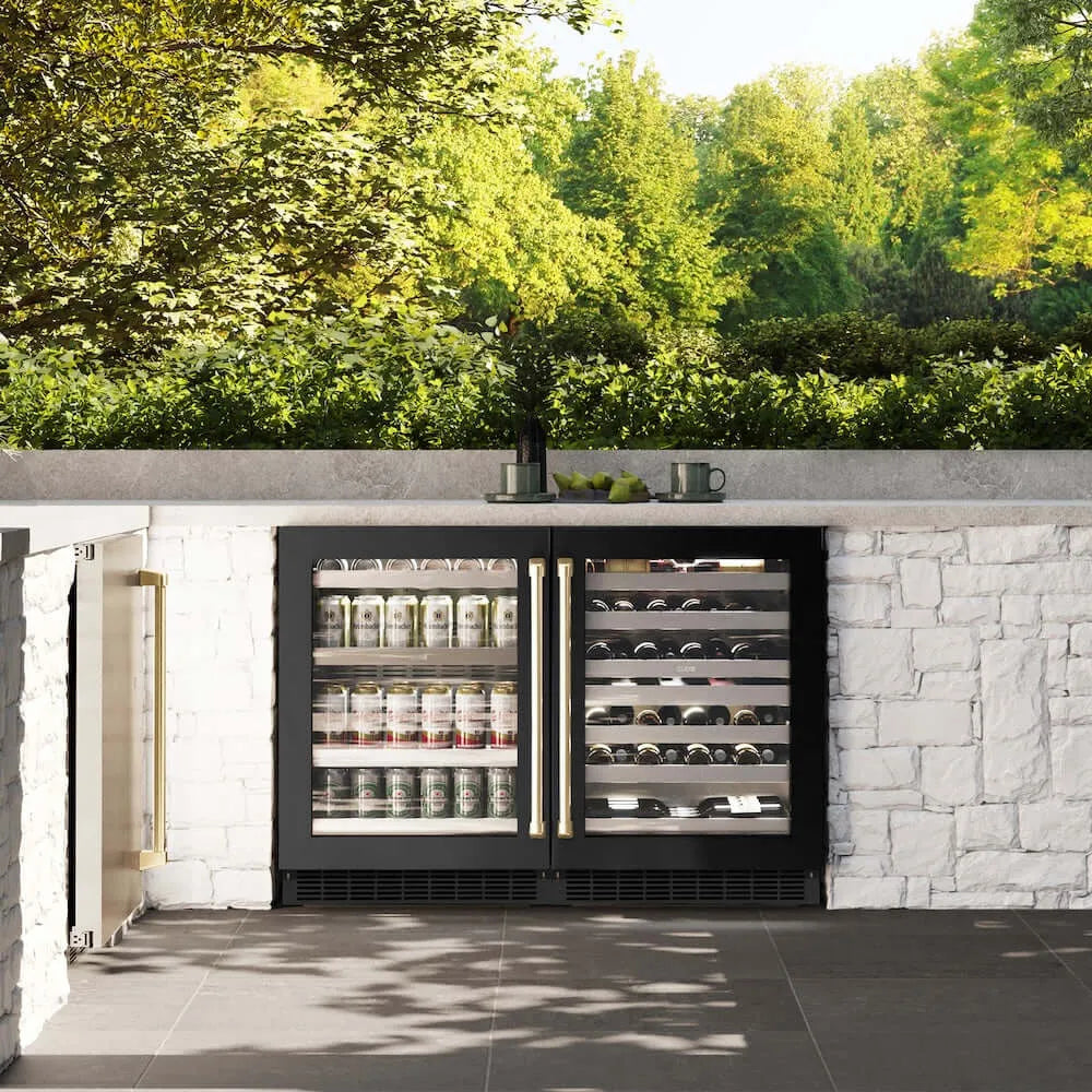 ZLINE Autograph Edition 24 in. Touchstone 151 Can Beverage Fridge With Black Stainless Steel Glass Door And Champagne Bronze Handle (RBSOZ-BS-24-CB) front, in an outdoor patio area with a matching wine cooler against a stone wall and greenery.