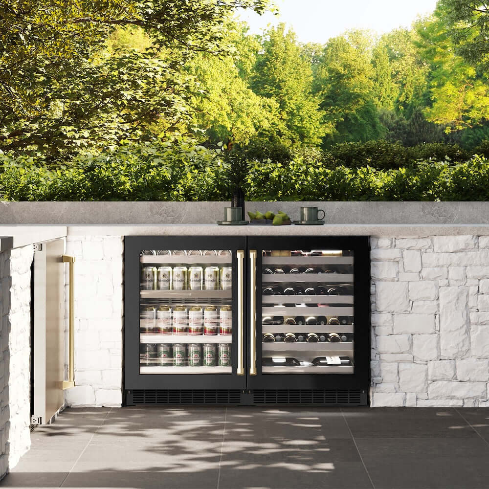 ZLINE Autograph Edition 24 in. Touchstone 151 Can Beverage Fridge With Black Stainless Steel Glass Door And Champagne Bronze Handle (RBSOZ-BS-24-CB) front, in an outdoor patio area with a matching wine cooler against a stone wall and greenery.