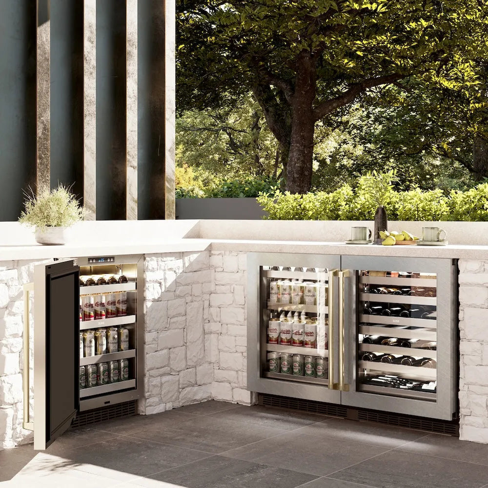ZLINE Autograph Edition 24 in. Touchstone 151 Can Beverage Fridge With Satin Stainless Steel Glass Door And Champagne Bronze Handle (RBSOZ-SN-24-CB) side, in an outdoor patio area against a stone wall and greenery.