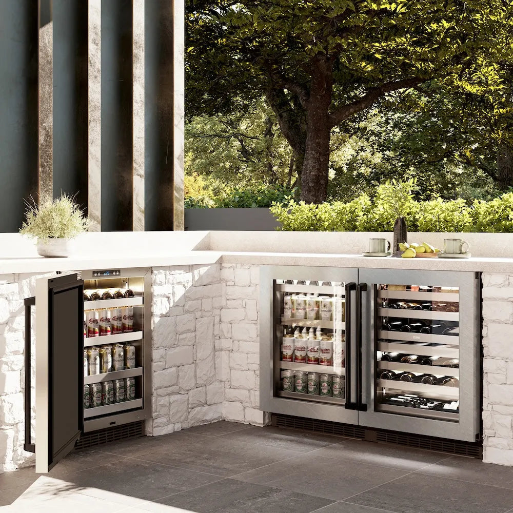 ZLINE Autograph Edition 24 in. Touchstone 151 Can Beverage Fridge With Satin Stainless Steel Glass Door And Matte Black Handle (RBSOZ-SN-24-MB) side, in an outdoor patio area against a stone wall and greenery.