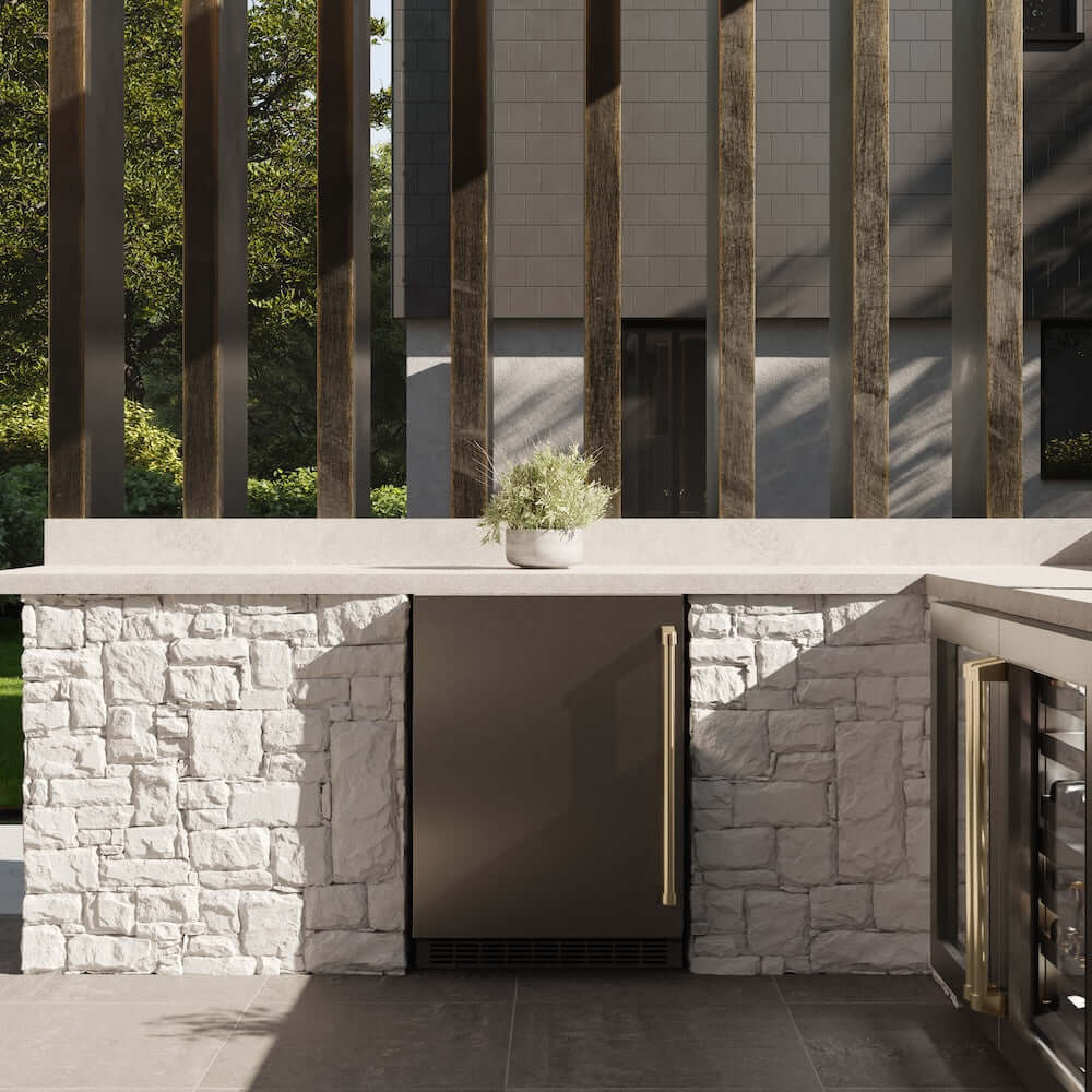 ZLINE Autograph Edition 24 in. Touchstone 151 Can Beverage Fridge With Solid Stainless Steel Door And Champagne Bronze Handle (RBSOZ-ST-24-CB) front, in an outdoor patio area with a matching wine cooler against a stone wall and greenery.
