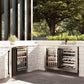 Outdoor kitchen with ZLINE Autograph Edition 24 in. Touchstone Dual Zone 44 Bottle Wine Cooler with Stainless Steel Glass Door and Matte Black Handle (RWDOZ-GS-24-MB) against a stone wall and greenery.