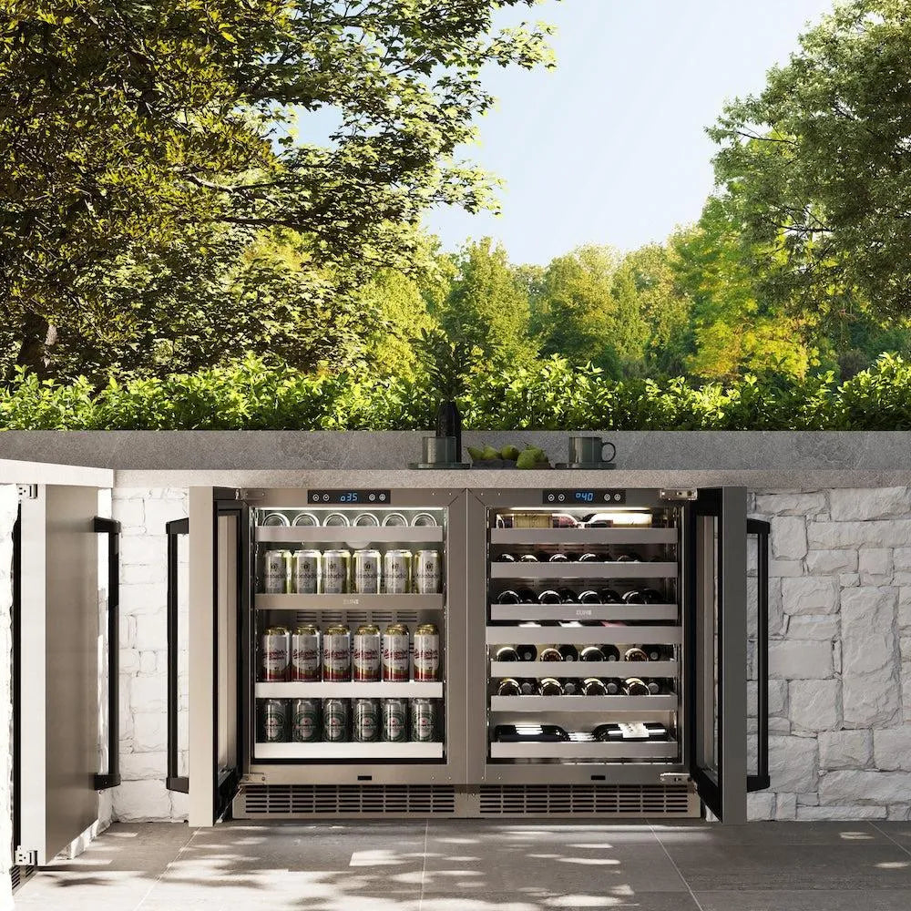 Outdoor kitchen with a ZLINE Autograph Edition 24 in. Touchstone Dual Zone 44 Bottle Wine Cooler with Stainless Steel Glass Door and Matte Black Handle (RWDOZ-GS-24-MB) filled with bottles and cans, surrounded by trees.