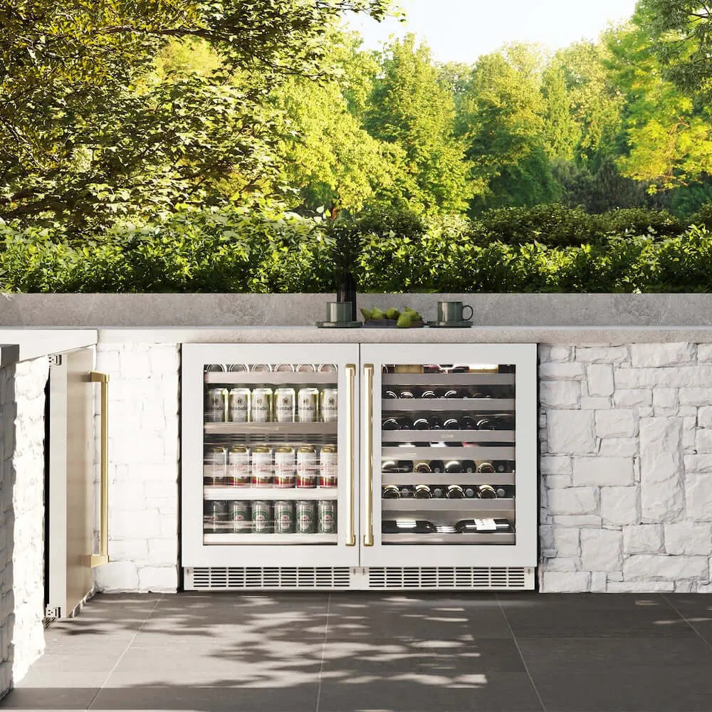 ZLINE Autograph Edition 24 in. Touchstone 151 Can Beverage Fridge With White Matte Glass Door And Champagne Bronze Handle (RBSOZ-WM-24-CB) front, in an outdoor patio area with a matching wine cooler against a stone wall and greenery.
