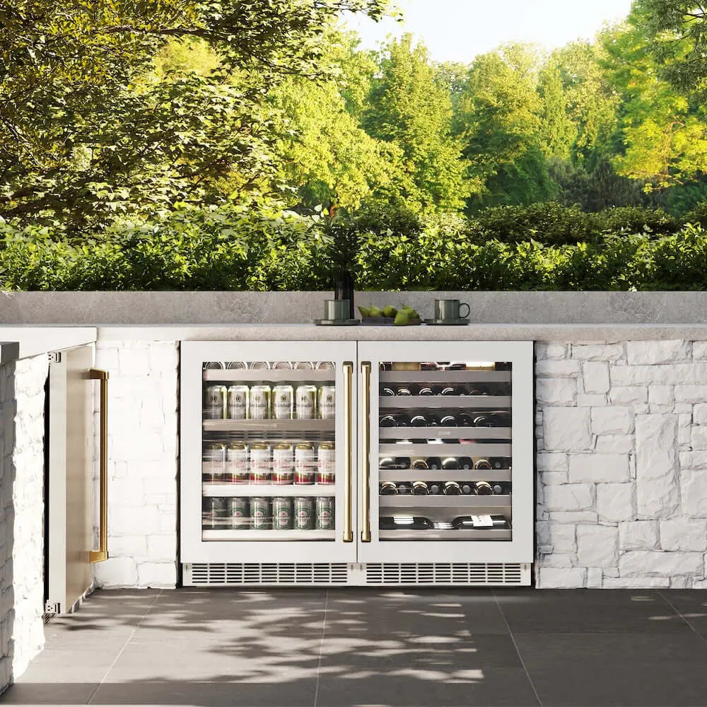 ZLINE Autograph Edition 24 in. Touchstone 151 Can Beverage Fridge With White Matte Glass Door And Polished Gold Handle (RBSOZ-WM-24-G) front, in an outdoor patio area with a matching wine cooler against a stone wall and greenery.