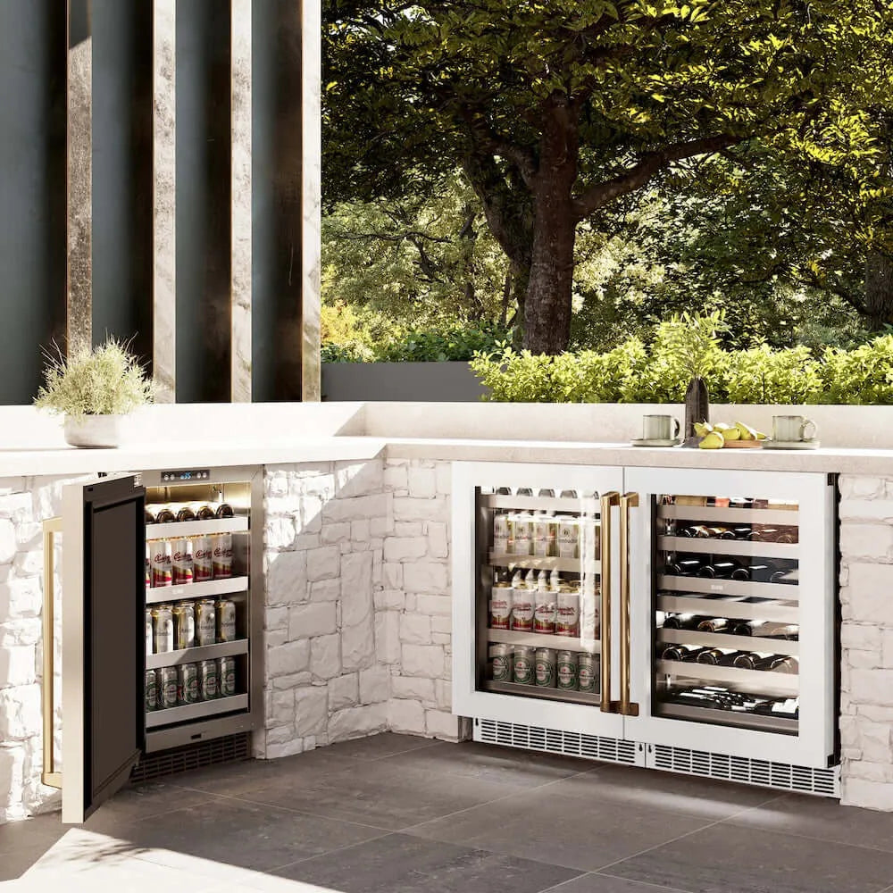 ZLINE Autograph Edition 24 in. Touchstone 151 Can Beverage Fridge With White Matte Glass Door And Polished Gold Handle (RBSOZ-WM-24-G) side, in an outdoor patio area against a stone wall and greenery.