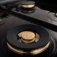 ZLINE Autograph Edition 24 in. 2.8 cu. ft. Legacy Dual Fuel Range with 4 Burner Gas Cooktop and Electric Convection Oven in Stainless Steel and Polished Gold Accents (RAZ-24-G) close-up, brass burners on black porcelain cooktop with no grates.