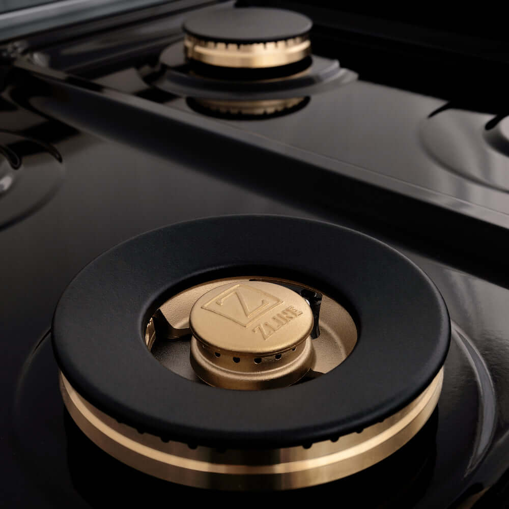 ZLINE Autograph Edition 24 in. 2.8 cu. ft. Legacy Dual Fuel Range with 4 Burner Gas Cooktop and Electric Convection Oven in Stainless Steel and Polished Gold Accents (RAZ-24-G) close-up, brass burners on black porcelain cooktop with no grates.