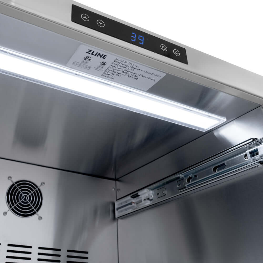ZLINE Autograph Edition 24 in. Touchstone 168 Can Outdoor-Rated Dual Refrigerator Drawer with Panel-Ready Doors and Champagne Bronze Handles (RDSPOZ-24-CB) close-up, LED light in interior.