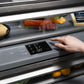 ZLINE Autograph Edition 30 in. 16.1 cu. ft. Built-In Bottom Freezer Refrigerator with Water Dispenser and Ice Maker in Black Stainless Steel with Graphite Gray Interior and Polished Gold Helix Handles (GRBIVZ-BS30KG) hand adjusting digital temperature control inside refrigeration compartment with food items inside.