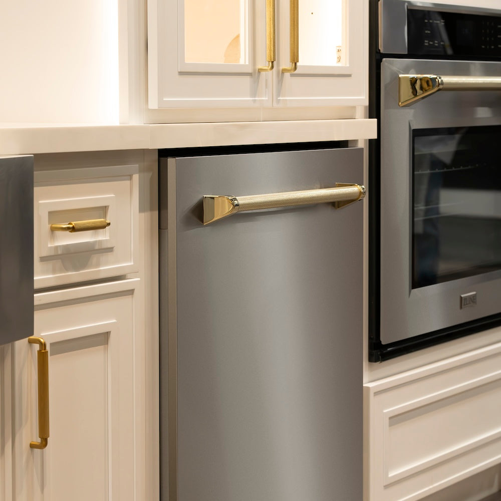 ZLINE Autograph Edition 24 in. Monument Series 3rd Rack Top Touch Control Tall Tub Dishwasher in Stainless Steel with Polished Gold Helix Handle, 45dBa (DWMTZ-30424-KG) in a kitchen with stainless steel wall oven and white cabinets with matching knurled cabinet pulls.