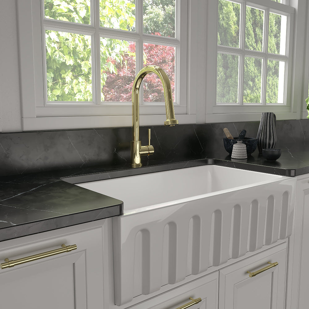 ZLINE Monet Kitchen Faucet (MON-KF) Polished Gold in a kitchen with a white farmhouse sink and black countertops.