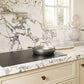A ZLINE 30 in. Induction Cooktop with Anti-Scratch Glass and 4 Elements (FCIND-30) with a silver pan and lid on a white and gray marble countertop in a bright kitchen setting.