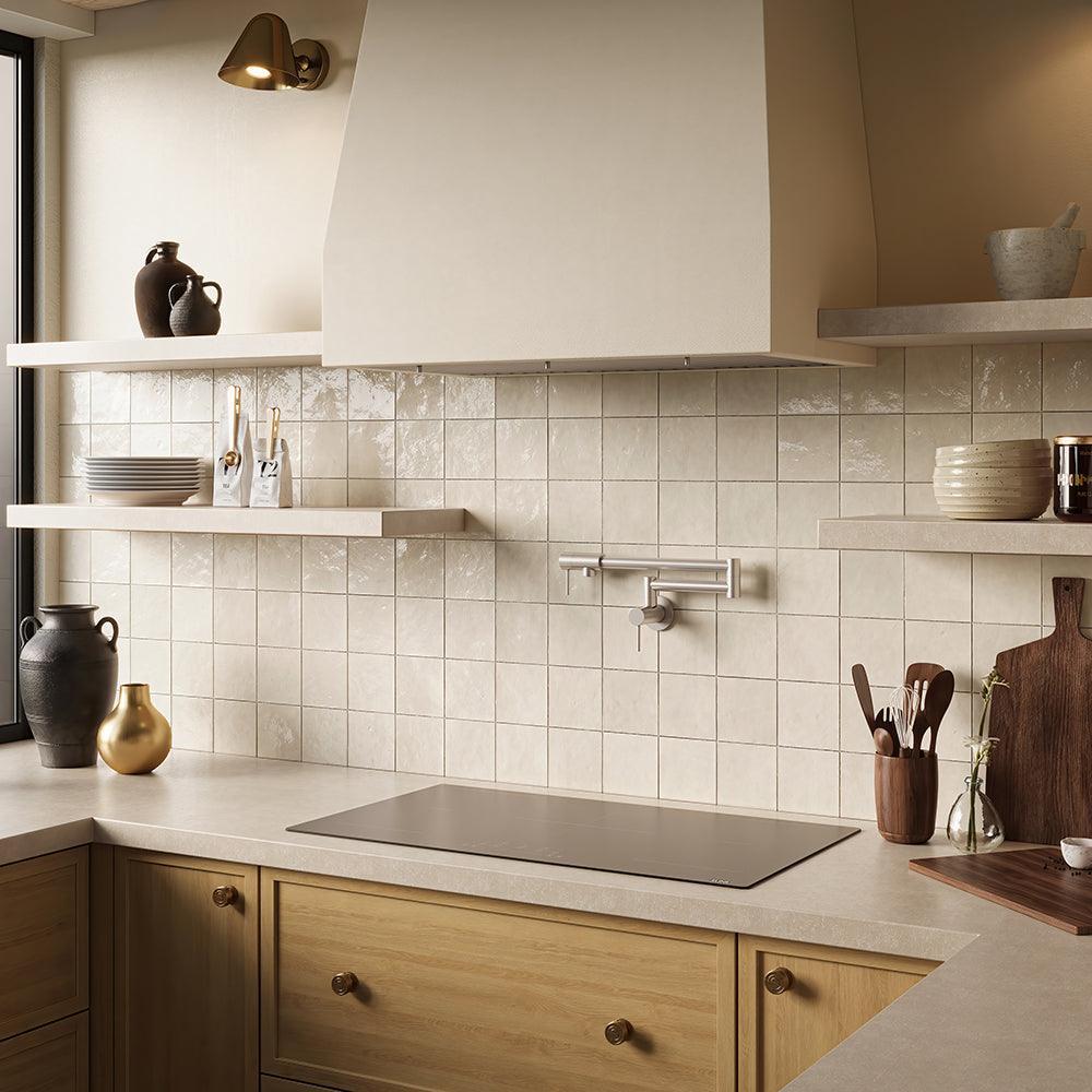 A modern kitchen interior with cream subway tile backsplash, light wood cabinetry, open floating shelves with ceramic vessels, a ZLINE 36 in. Induction Cooktop with Anti-Scratch Glass and 5 Elements (FCIND-36), and a large cream range hood.