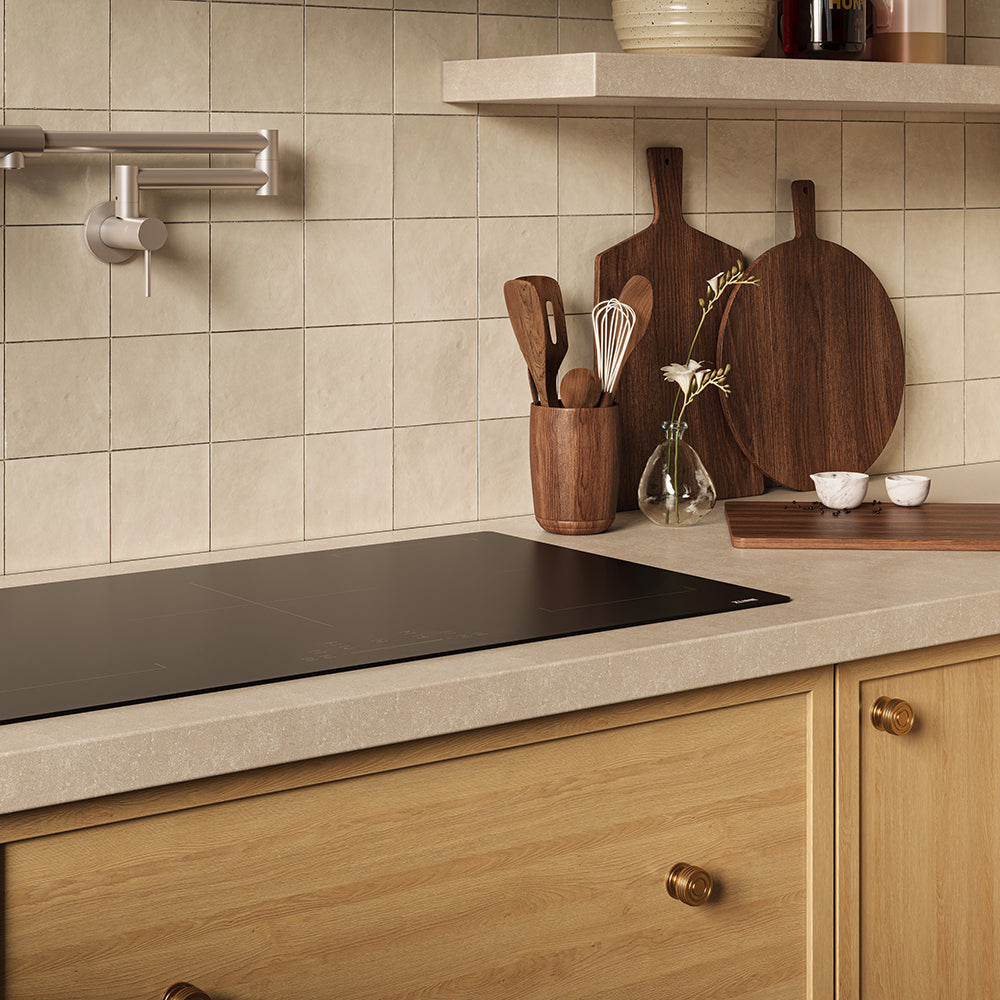 A modern kitchen scene with a ZLINE 36 in. Induction Cooktop with Anti-Scratch Glass and 5 Elements (FCIND-36), beige tiled backsplash, light wood cabinets, and dark wood cutting boards and utensils on the counter.