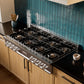 ZLINE 48 in. Classic Gas Rangetop with 8 Burner DuoPro™ Cooktop in Stainless Steel (PCRT48) in a kitchen with wooden cabinets, a custom range hood, and a blue-green tiled backsplash, angled.