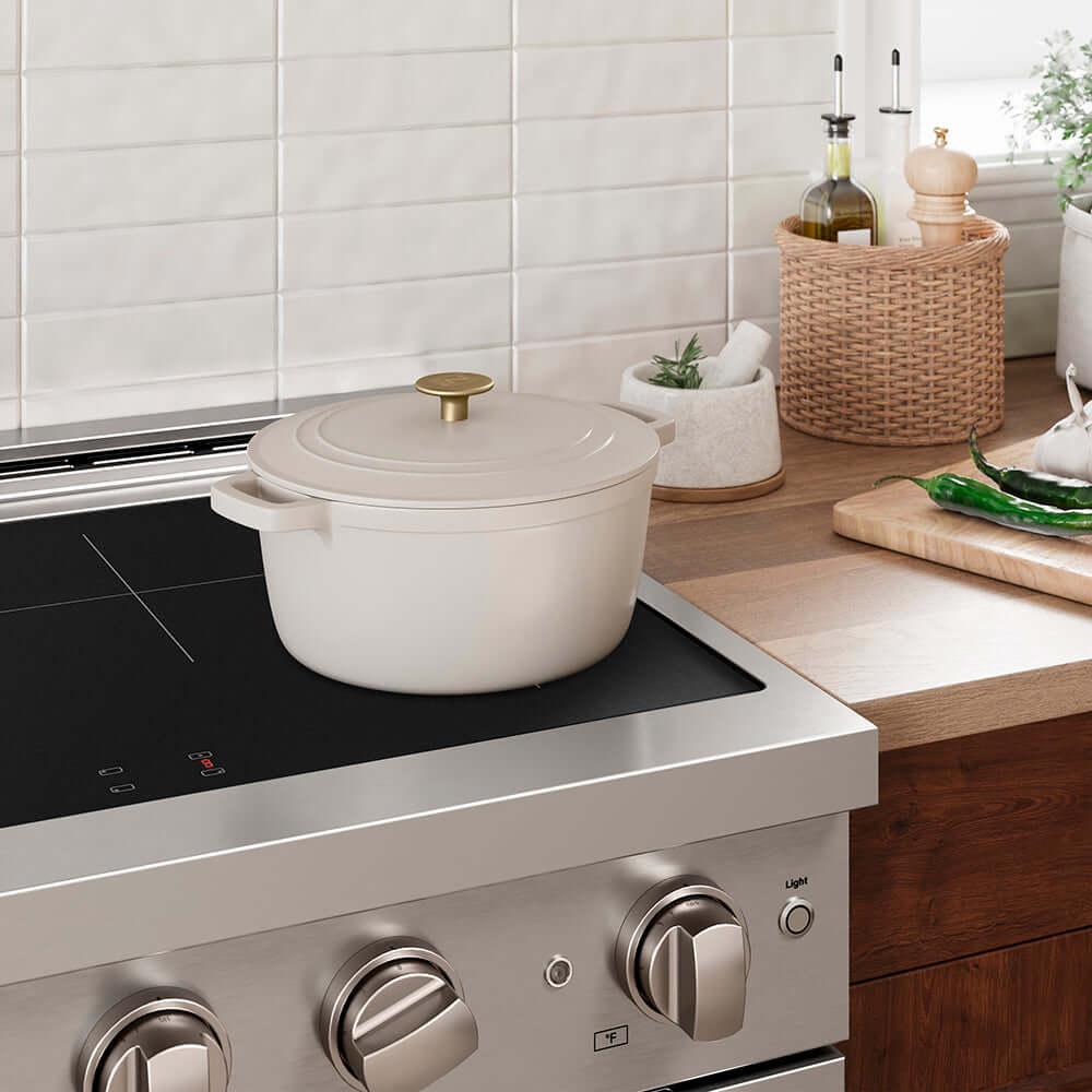White enameled cast iron pot on a modern induction range in a kitchen with wooden cabinets and decorative items.