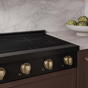 A close-up of a ZLINE Autograph Edition 30 in. Paramount Induction Rangetop with 4 Element Cooktop in Black Stainless Steel and Champagne Bronze Accents (SINRTBZ-30-CB) set into a brown kitchen cabinet beneath a white marble countertop and backsplash.
