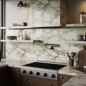 A modern kitchen interior with a white marble backsplash and matching marble countertops, dark wood cabinetry, a ZLINE Autograph Edition 36 in. Paramount Induction Rangetop with 5 Element Cooktop in Satin Stainless Steel and Matte Black Accents (SINRTSZ-36-MB), floating shelves with dishes, and a black wall-mounted faucet.