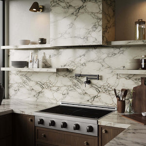 A modern kitchen interior featuring a white marble backsplash with dramatic gray veining, matching marble countertops, dark wood cabinetry, a ZLINE Autograph Edition 36 in. Paramount Induction Rangetop with 5 Element Cooktop in Stainless Steel and Matte Black Accents (SINRTZ-36-MB), floating open shelves with ceramic dishes, and a matte black faucet.