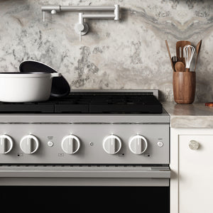 ZLINE 30 in. 4.2 cu. ft. Marino Gas Range with Convection Gas Oven in Stainless Steel with 4 Brass Burners (MGR-BR-30) front close-up, set in a modern kitchen with marble countertops. A white pot sits on the cooktop, and a wooden utensil holder is on the counter.