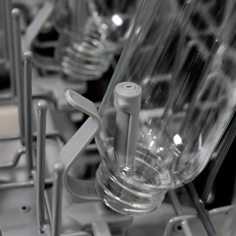 Close-up of a clear glass bottle on a bottle jet inside a ZLINE Autograph Edition 24 in. Monument Series 3rd Rack Dishwasher with Auto Door Open Drying, 44dBa, Black Stainless Steel Panel with Champagne Bronze Helix Handle (DWMTZ-BS-24-KCB).