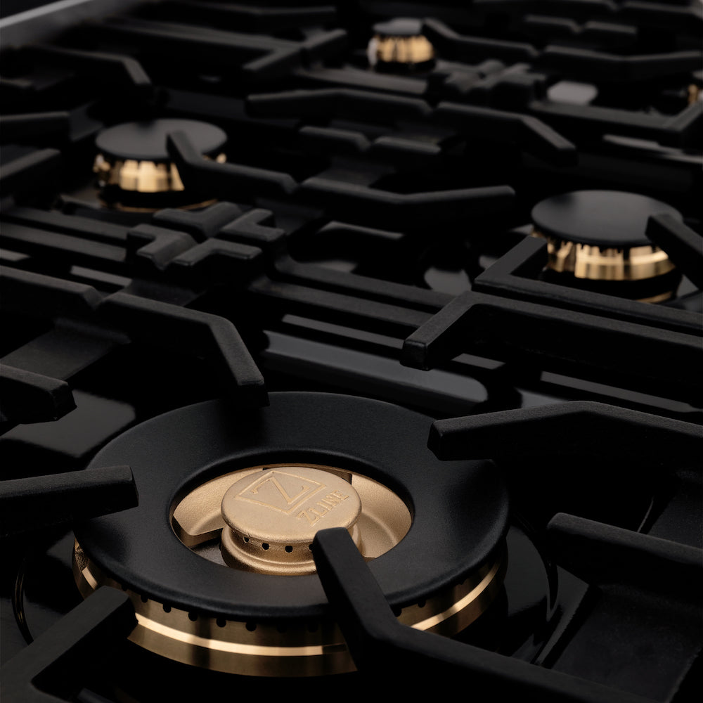 ZLINE Autograph Edition 36 in. 4.6 cu. ft. Legacy Dual Fuel Range with 6 Burner Gas Cooktop and Electric Convection Oven in Black Stainless Steel and Champagne Bronze Accents (RABZ-36-CB) close-up, brass burners on black porcelain cooktop with no grates.