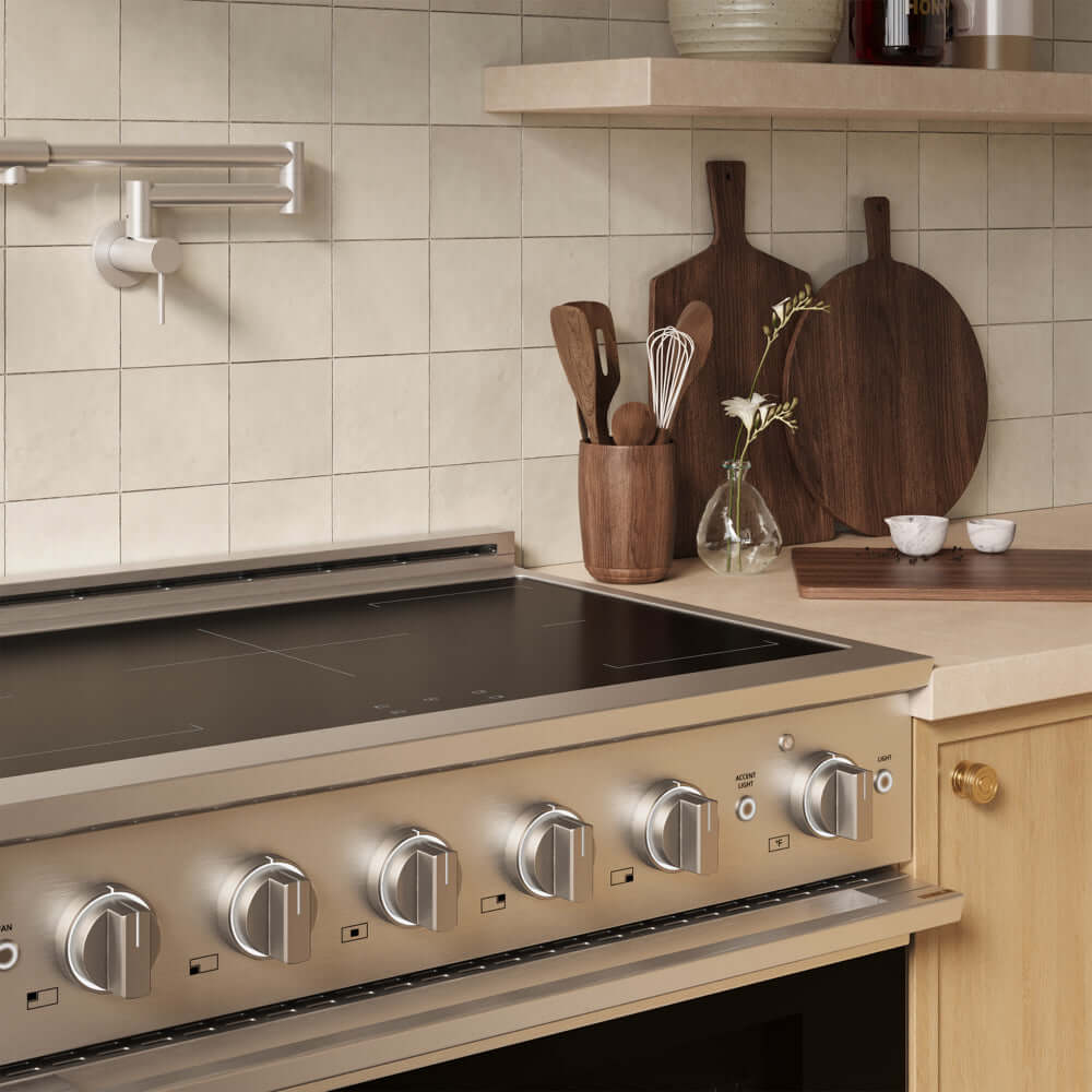 A ZLINE 36 in. 5.2 cu. ft. Marino Induction Range with 5 Element Cooktop and Electric Convection Oven in Stainless Steel (MINR36), set into a light wood kitchen cabinet. The background features beige square tiles, a wooden shelf, and dark wood cutting boards on the countertop.
