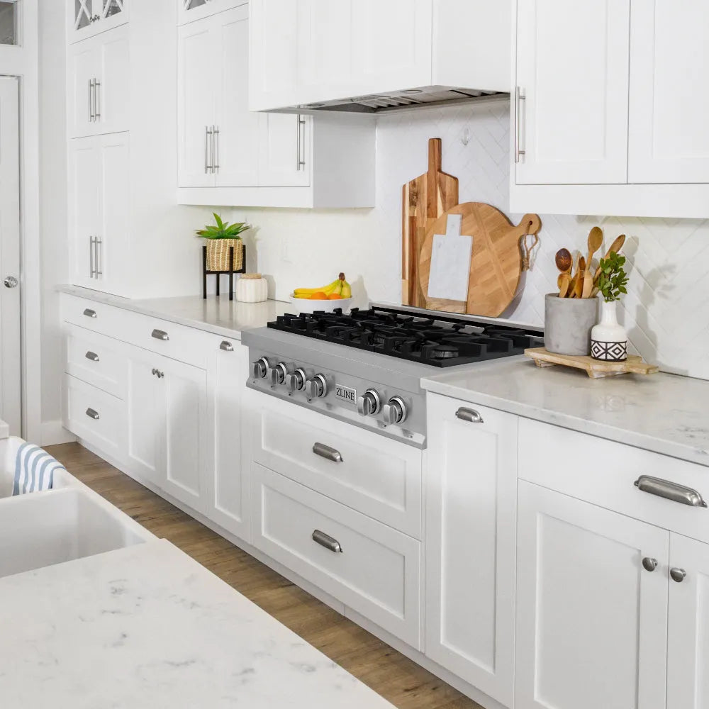 Farmhouse kitchen with white cabinets, marble countertops, and stainless steel rangetop.