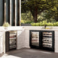 ZLINE 24 in. Touchstone 151 Can Beverage Fridge With Black Stainless Steel Glass Door (RBSO-BS-24) side, in an outdoor patio area against a stone wall and greenery.