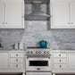 ZLINE Designer Series Satin Stainless Steel Convertible Vent Wall Mount Range Hood (8KBS) in a kitchen with white cabinets, marble backsplash, and a blue pot on the range.