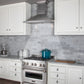 ZLINE Designer Series Satin Stainless Steel Convertible Vent Wall Mount Range Hood (8KBS) in a kitchen with white cabinets, marble backsplash, and a blue pot on the range.