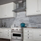 ZLINE Designer Series Satin Stainless Steel Convertible Vent Wall Mount Range Hood (8KBS) in a kitchen with white cabinets, marble backsplash, and a blue pot on the range.