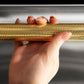 ZLINE Autograph Edition 24 in. Monument Series 3rd Rack Dishwasher with Auto Door Open Drying, 44dBa, Stainless Steel Panel with Polished Gold Helix Handle (DWMTZ-30424-KG), close-up, person holding Helix handle showing knurled diamond texture.