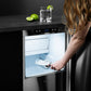 ZLINE Autograph Edition 15 in. Touchstone Gourmet Ice Maker with Drain Pump and Solid Stainless Steel Door with Polished Gold Helix Handle (IGMDZ-ST-15-KG) person using stainless steel ice scoop to scoop ice with a glass of water and limes on the counter.