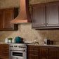 ZLINE Designer Series Hand-Hammered Copper Wall Mount Range Hood in a rustic kitchen with brown cabinets side.