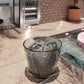 A clear textured glass tumbler containing clear cube ice made with a ZLINE 15 in. Touchstone Clear Cube Ice Maker with Drain Pump and Solid Stainless Steel Door (ICCD-ST-15) placed on a stone patio near a poolside bar area.